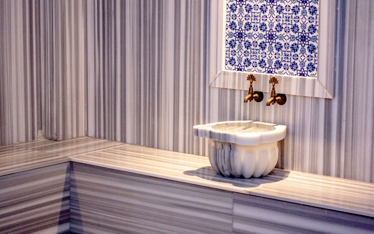 Interior of a traditional Turkish hamam featuring marble and mosaic tiles with brass faucets
