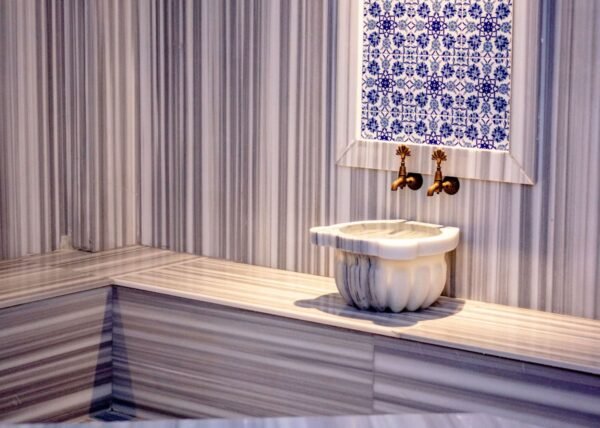 Interior of a traditional Turkish hamam featuring marble and mosaic tiles with brass faucets